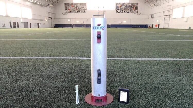 Advanced Artificial Athlete drop test tower standing on an indoor artificial grass pitch
