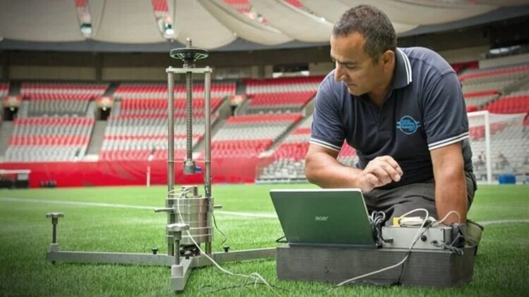 Sports Labs technician working at a laptop with test equipment beside a stadium pitch
