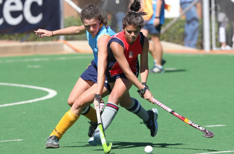 Two field hockey players competing for the ball on a green synthetic pitch