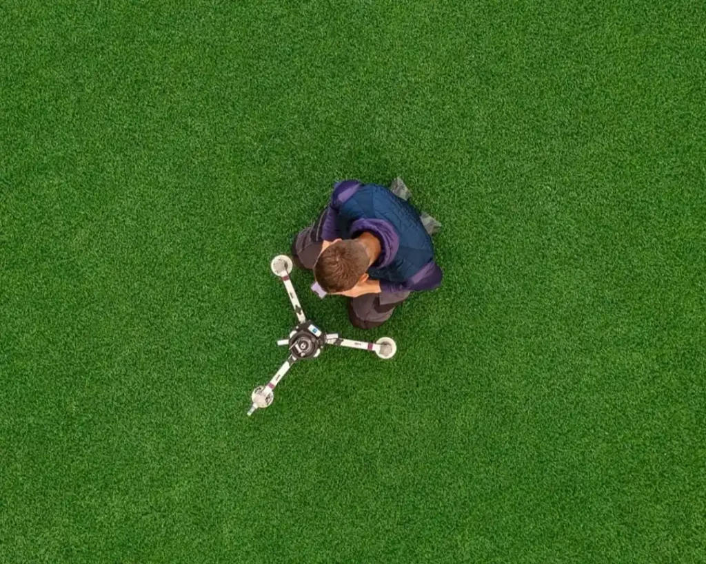 Overhead view of a technician operating a three legged impact test device on a green pitch