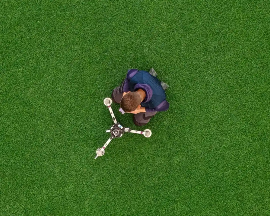 Overhead view of a technician operating a three legged impact test device on a green pitch