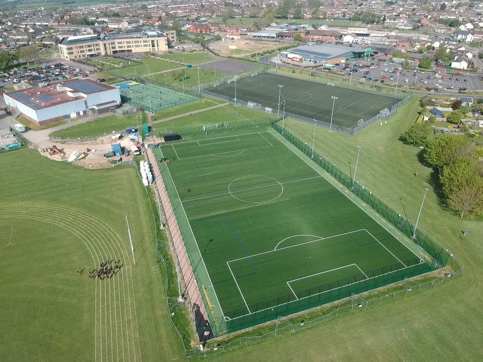 Aerial view of a floodlit 3G artificial grass pitch beside a leisure complex