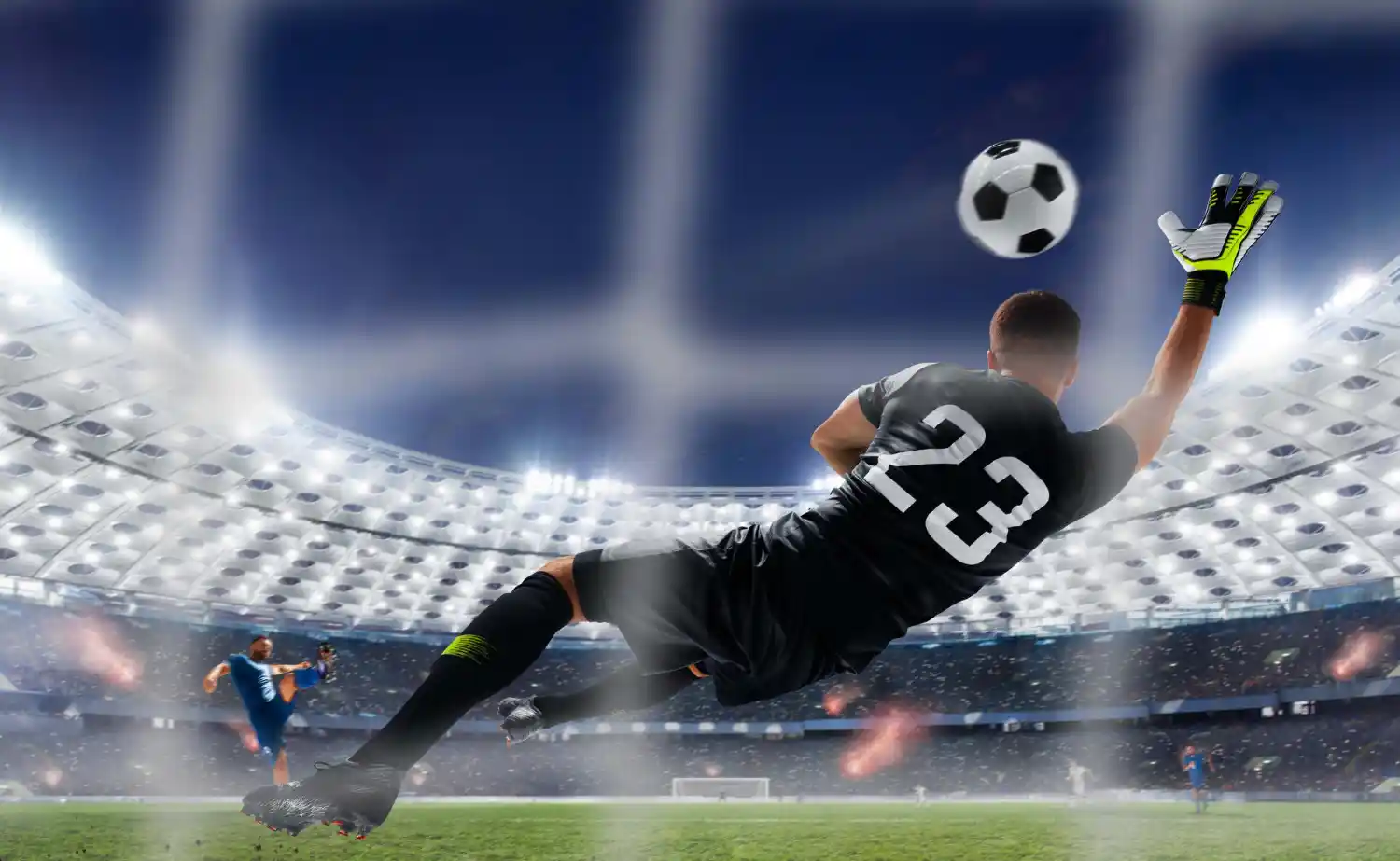 Goalkeeper diving to reach a football in front of a floodlit stadium crowd