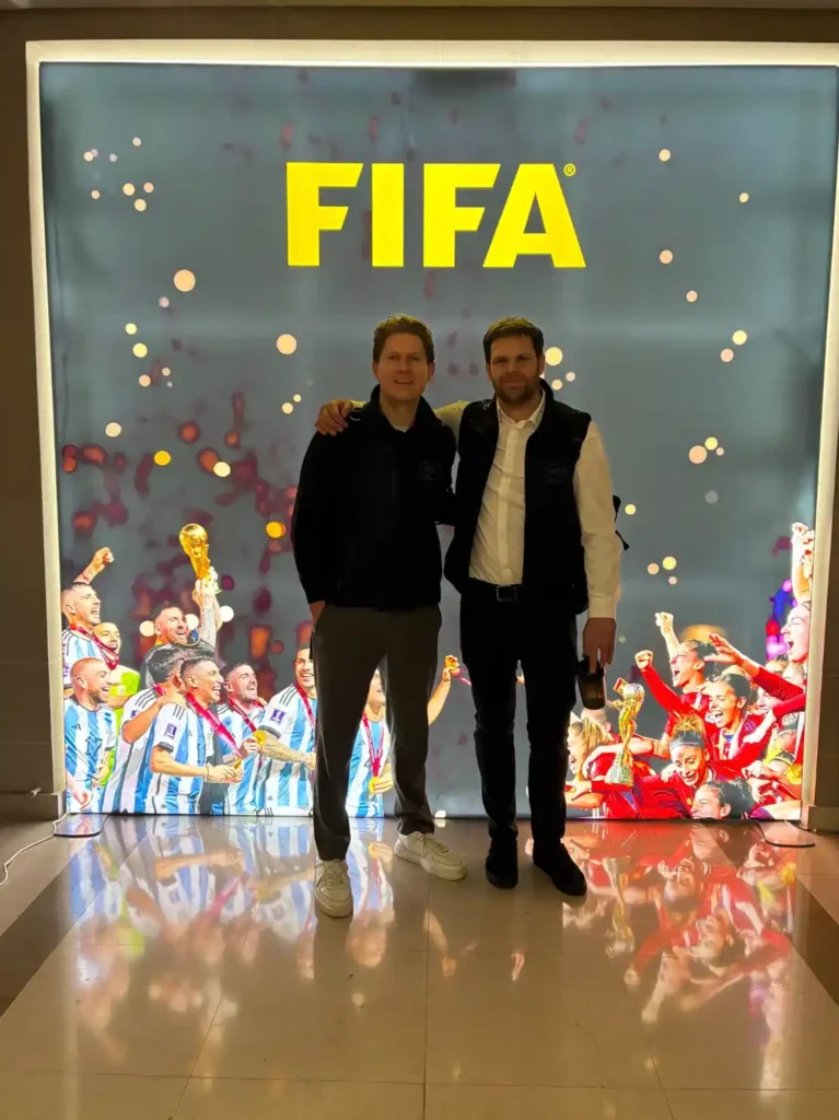 Two members of the Sports Labs team at a FIFA branded event with award trophies on display