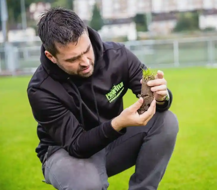 Sports Labs technician crouching on a natural turf pitch with test equipment