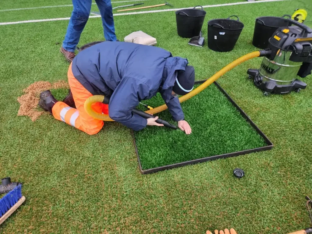 Sports Labs technician vacuuming performance infill from a marked test square on a 3G pitch to retest drainage