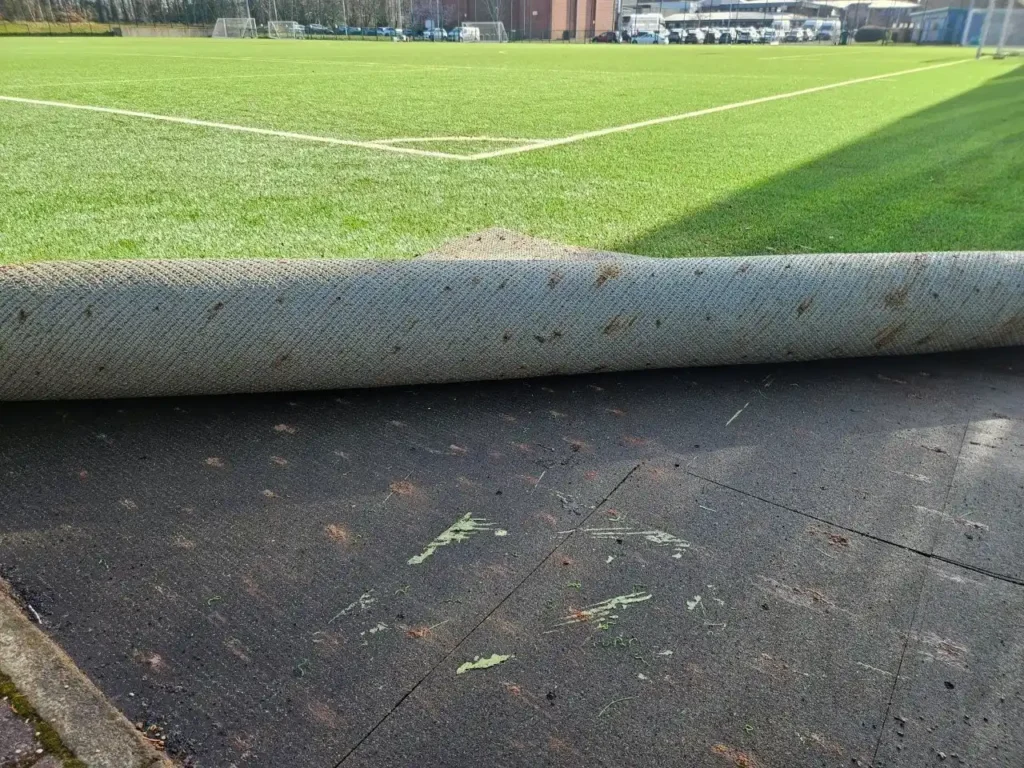 Artificial pitch carpet rolled back revealing the bitmac engineered base with the 3G playing surface behind