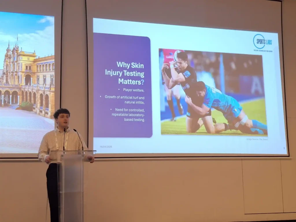 Speaker presenting a talk titled Why Sports Injury Testing Matters to a conference audience