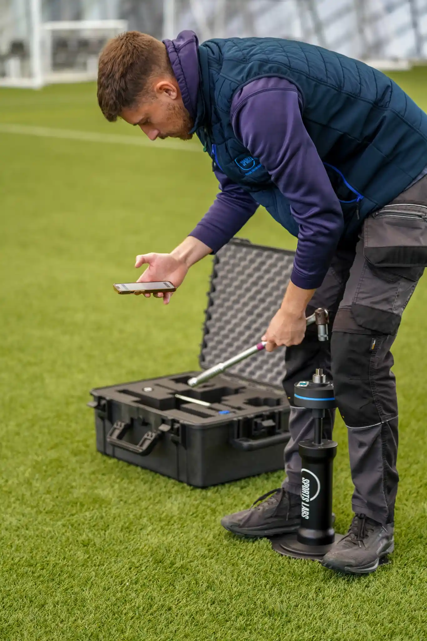 Groundsman kneeling on a natural turf pitch beside the open ProPitch Standard Kit case